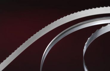 Simmons' most popular food processing bandsaw blades curve and catch the light in front of a dark background.