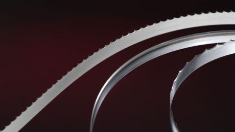 Simmons' most popular food processing bandsaw blades curve and catch the light in front of a dark background.
