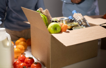 A cardboard box filled with produce, canned food, and water bottles.