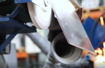A Simmons grinding wheel runs at high speed while sparks fly in the background.